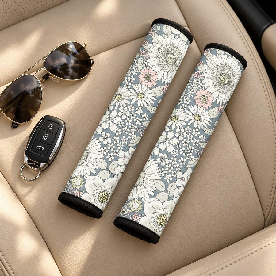 Snowy Field Of Flowers Seat Belt Covers (Set of 2) lying side by side on a tan leather car seat with sunglasses and a car key