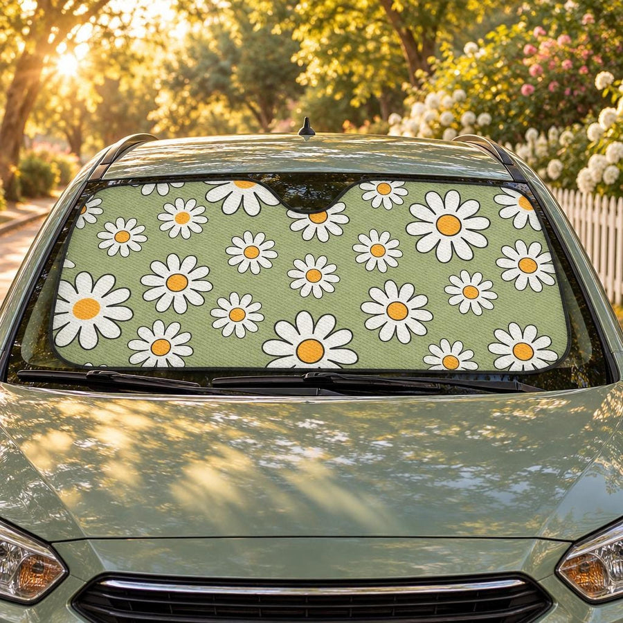 Sage Green Daisy Car Shade fitted in the windscreen of a sage-green hatchback on a leafy street at golden hour, printed side facing out