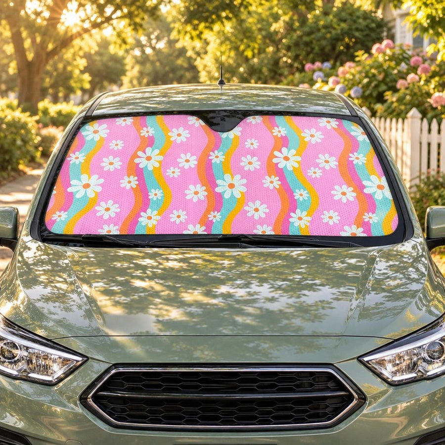 Pink Groovy Flowers Car Shade fitted in the windscreen of a sage-green hatchback on a leafy street at golden hour, printed side facing out