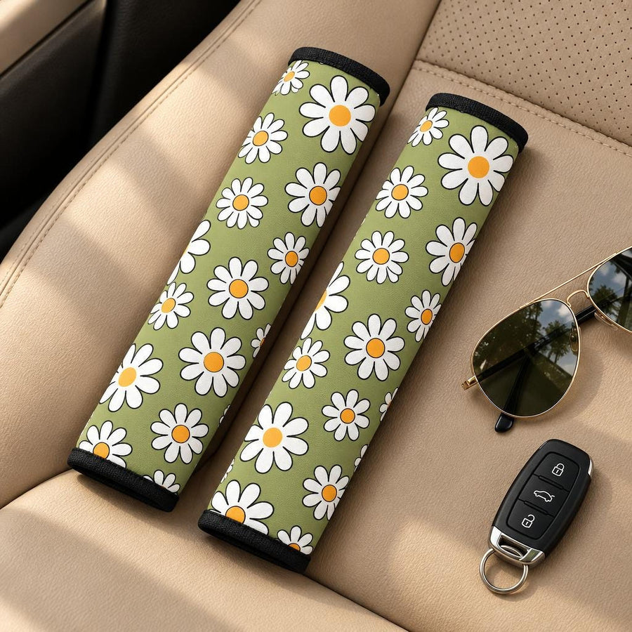 Sage Green Daisy Seat Belt Covers (Set of 2) lying side by side on a tan leather car seat with sunglasses and a car key